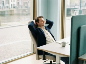 Ontspannen ondernemer in ergonomische stoel met handen achter het hoofd in een rustig, minimalistisch Nederlands kantoor met natuurlijk licht.